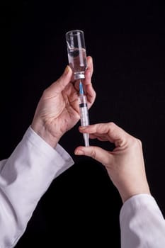 Filling of a syringe with medicine from vial. Medical person holding medical syringe and drug vial. Tip of needle shows. Isolated Black background.