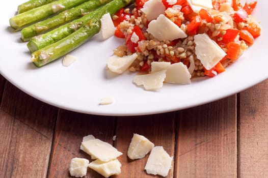 Vegetarian buckwheat risotto with red Bell peppers, served with grilled fresh green organic asparagus and garnished with fresh parmesan cheese