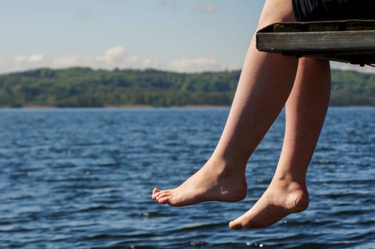 Pair of legs hanging over the edge of a Lake jetty.