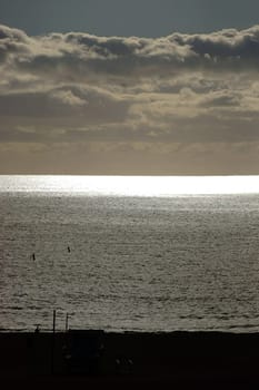 The silhouette of a jogger and a guardhouse in the evening on the beach with sun reflections in the water.