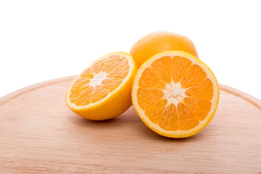 Approach and presentation of an orange split in half and a full in the back. They are on a wooden plate and white background