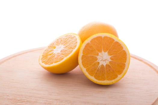 Approach and presentation of an orange split in half and a full in the back. They are on a wooden plate and white background