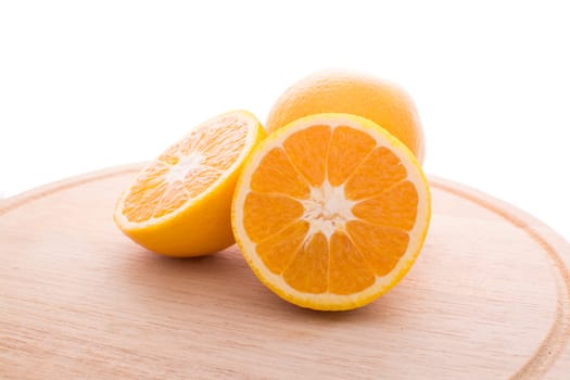 Approach and presentation of an orange split in half and a full in the back. They are on a wooden plate and white background
