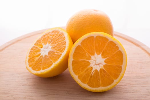 Approach and presentation of an orange split in half and a full in the back. They are on a wooden plate and white background