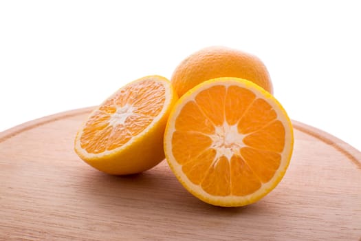 Approach and presentation of an orange split in half and a full in the back. They are on a wooden plate and white background