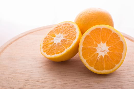 Approach and presentation of an orange split in half and a full in the back. They are on a wooden plate and white background
