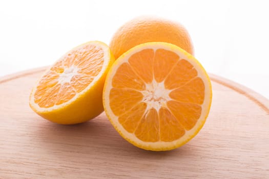 Approach and presentation of an orange split in half and a full in the back. They are on a wooden plate and white background