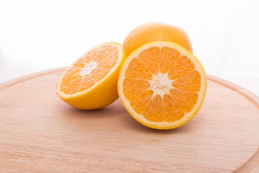 Approach and presentation of an orange split in half and a full in the back. They are on a wooden plate and white background