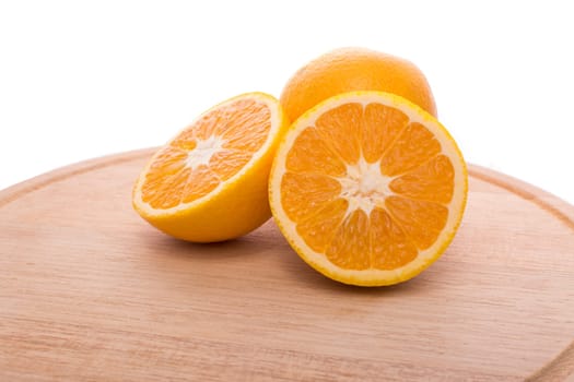 Approach and presentation of an orange split in half and a full in the back. They are on a wooden plate and white background