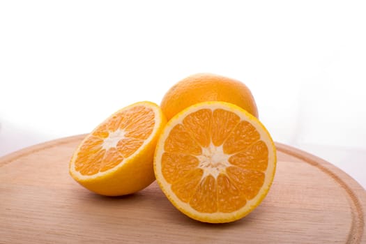 Approach and presentation of an orange split in half and a full in the back. They are on a wooden plate and white background