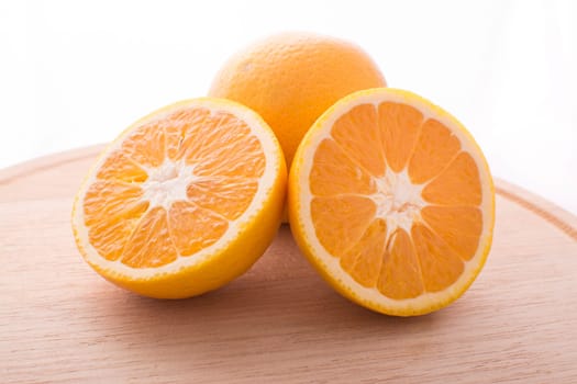 Approach and presentation of an orange split in half and a full in the back. They are on a wooden plate and white background