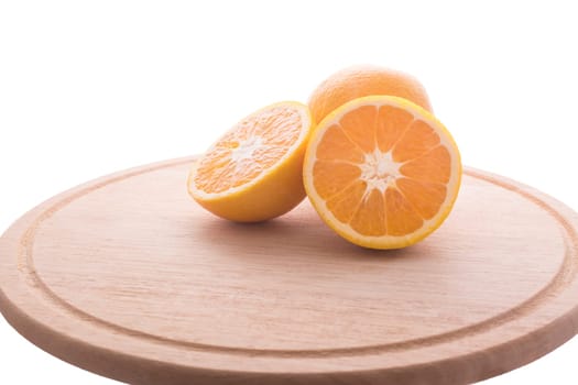Approach and presentation of an orange split in half and a full in the back. They are on a wooden plate and white background