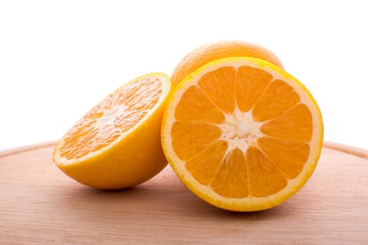 Approach and presentation of an orange split in half and a full in the back. They are on a wooden plate and white background
