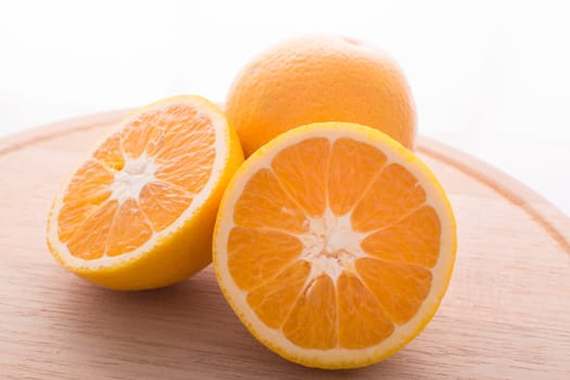 Approach and presentation of an orange split in half and a full in the back. They are on a wooden plate and white background