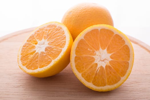 Approach and presentation of an orange split in half and a full in the back. They are on a wooden plate and white background