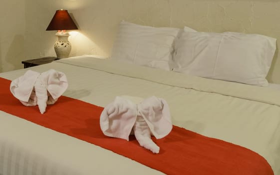 White towel in elephant shape on white bed in Thai style hotel bedroom