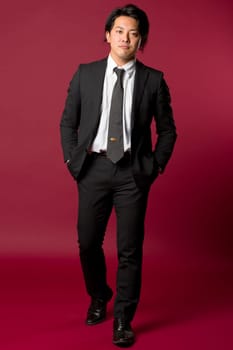 A portrait of a young Japanese man in a business suit walking on a red background.