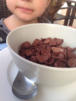Child girl having a healthy breakfast outdoors. She is eating chocolate flakes and orange juice