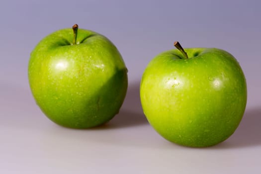 Pair of Granny Smith Apples side by side with some water drops on them.