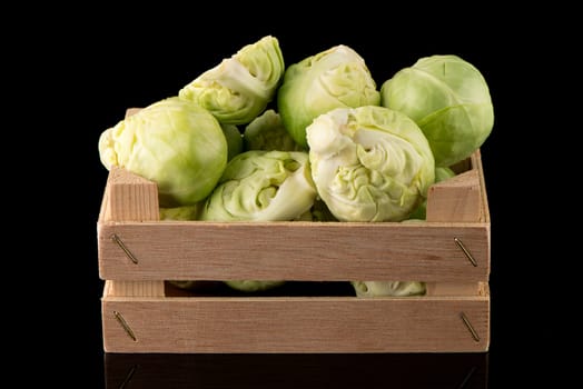 Fresh brussels sprouts on wooden box isolated on black background.