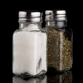 Salt and oregano shakers on black Background.