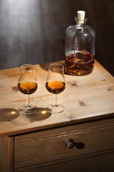 Bottle and two glasses of brandy on a vintage wooden table with closed drawer