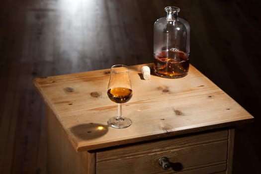 Bottle and a glass of brandy on a vintage wooden table with closed drawer