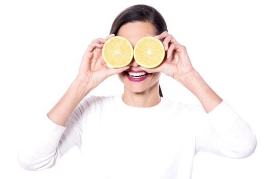 Happy young woman holding orange slices in front of eyes