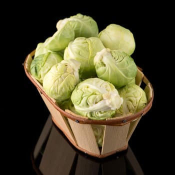 Fresh brussels sprouts and wooden baslet isolated on black background.