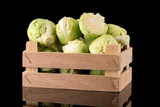 Fresh brussels sprouts on wooden box isolated on black background.