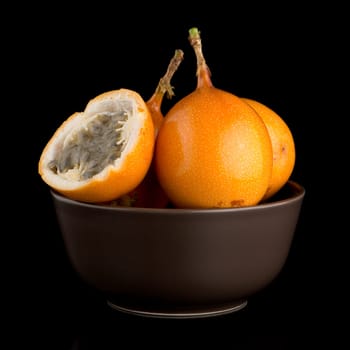 Passion fruit maracuja granadilla on ceramic brown bowl, black background.