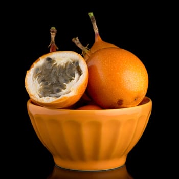 Passion fruit maracuja granadilla on ceramic yellow bowl, black background.
