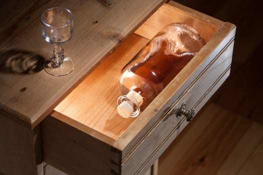Bottle brandy hidden in an antique wooden drawer and a drinking glass on the table