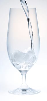 Water Pouring into Glass with Ice on white and grey background.