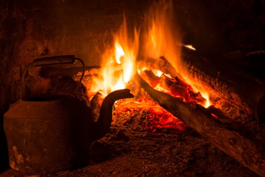 Old brick fireplace with burning wood and kettle. Winter time warm indoors scene.