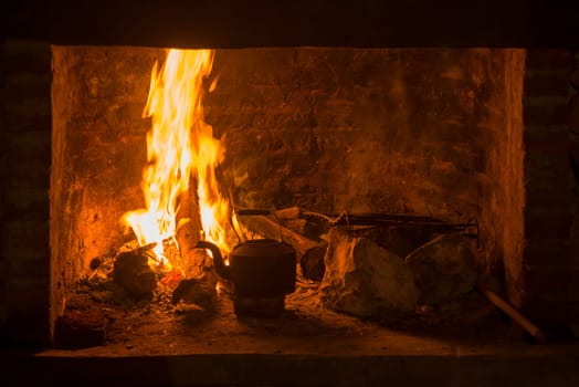 Traditional fireplace stove with fire burning and kettle. Winter time comfort concept.