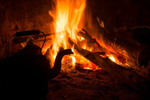 Winter time holiday scene with logs in old rustic fireplace burning and kettle.