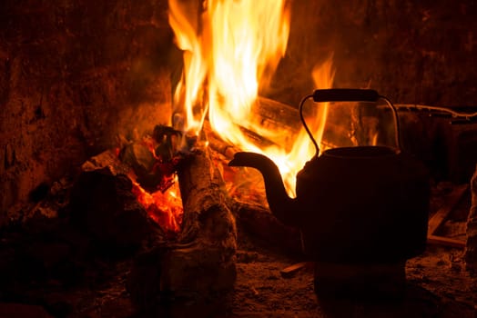 Kettle in fireplace, fire and wood burning. Cozy winter holiday cabin scene.