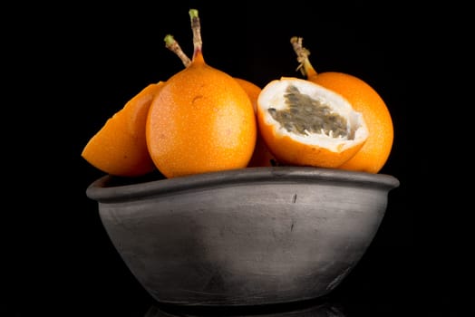 Passion fruit maracuja granadilla on ceramic black bowl, black background.