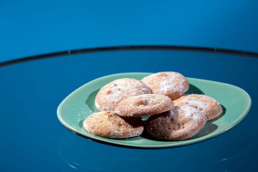 Butter lemon cookies on a green retro plate on a glass table with a blue background.