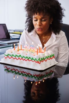 Business person celebrating 28 years and doing a party in office. She blows out the clandles on birthday cake and smiles for joy