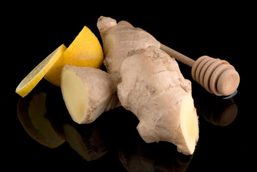 Ginger root drizzler with honey and lemon on black reflective background. Concept of natural ingredients to prevent colds.