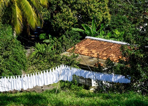 White Laundry hanging to dry outside with the roof of a House in the background and trees and Palms