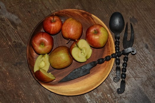 Apples on wooden plate with iron knife,spoon and fork next to it