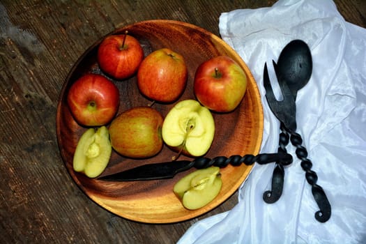 Apples on wooden plate with iron knife,spoon and fork next to it