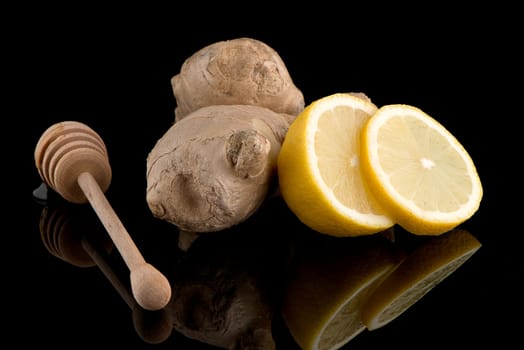 Ginger root drizzler with honey and lemon on black reflective background. Concept of natural ingredients to prevent colds.