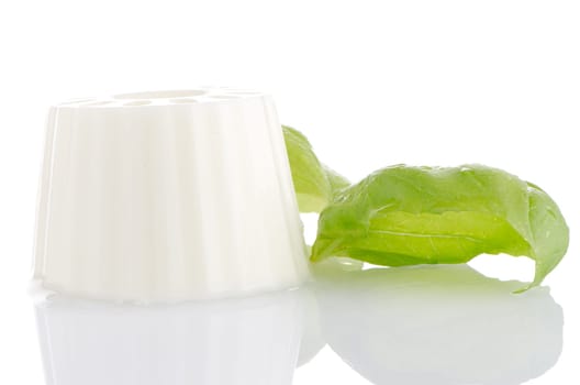 White fresh cheese with fresh basil leaves on white reflective background.