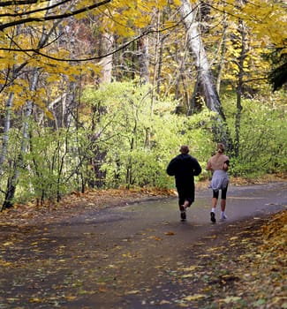 Man and woman running in the autumn forest on the way