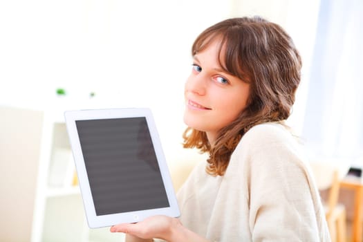 View of a young smiling woman using a tablet on a sofa