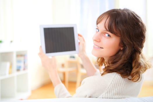 View of a young smiling woman using a tablet on a sofa
